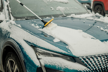 Cleaning Snow from a Car Hood with a Brush After Winter Snowfall