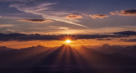 golden sun rays bursting through dramatic mountain peaks at sunset with contrails in the sky.