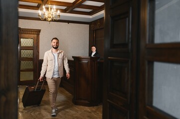 Man entering hotel lobby pulling suitcase for check in