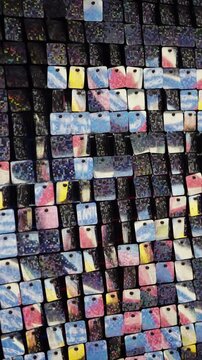 Shimmering mosaic of reflective square sequins forming an abstract, iridescent pattern with colorful gradients and glittering textures, creating a dynamic geometric wall installation