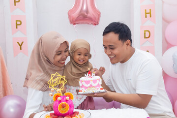 A happy Indonesian Muslim family celebrated their daughter's birthday with balloon and cake decorations.