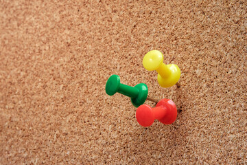 Colorful triple pushpins securely mark the corkboard surface. Utilizing selective focus to draw attention and leave generous text space for overlay design. Ideal for organization concepts.