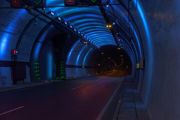 The vast, dark highway tunnel is strikingly illuminated by bright blue modern LED lights. Showcasing the smooth asphalt road leading into the distance. Ideal for transportation concepts.