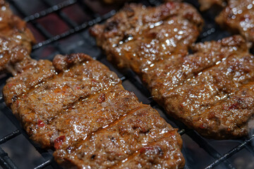 Ultra detail macro shot of juicy seasoned meat sizzling on a hot BBQ grill over dark charcoal and rising smoke. Perfect for menu design. Selective focus.