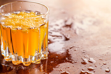 Vibrant glass of fresh orange fruit juice sits on a wet wooden table. Capturing the high detail and bright contrast of the healthy beverage. Ideal for food advertising. Selective focus.