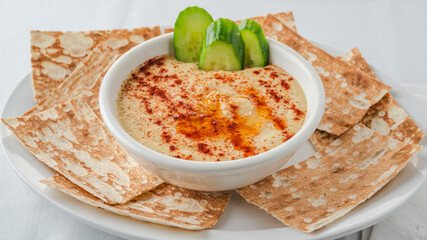 Hummus served with sliced cucumbers and lavash pieces arranged on a plate.