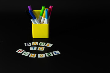 Back to school, markers and letters arranged on a black background, the beginning of school
