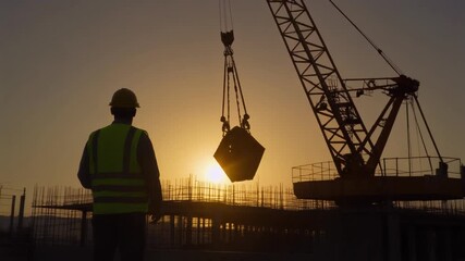 Dedicated construction worker in silhouette overseeing a large crane lifting heavy materials at a building site against a vibrant sunset, symbolizing progress and industrial development - Powered by Adobe