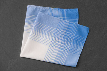 A folded blue and white patterned cotton handkerchief on a dark gray background.