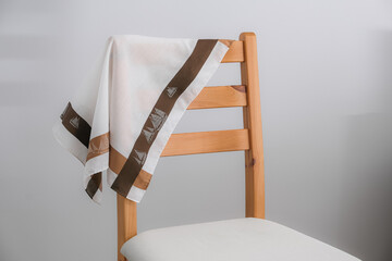 A white cotton handkerchief with a wide brown and tan border, featuring a sailboat pattern, is casually draped over the back of a light wooden chair with a white padded seat.