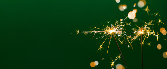 Fototapeta premium Bright golden sparks from two burning sparklers against a deep emerald green background with soft bokeh. A perfect background image for Christmas cards, New Year's banners, and holiday designs.