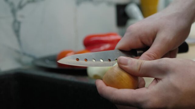 Process of peeling onion with sharp knife, showcasing culinary techniques and meticulous preparation in a kitchen, with fresh tomatoes beautifully arranged in the background