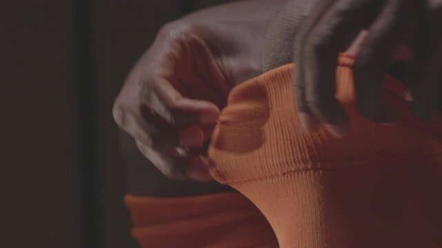 Close-up of an African American football player pulling up orange socks over his knees. The athlete is getting dressed and preparing for a soccer match in the locker room.


