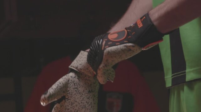 Close-up of an African American football player pulling up orange socks over his knees. The athlete is getting dressed and preparing for a soccer match in the locker room.

