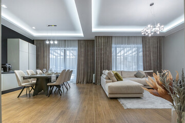 A spacious living and dining area with elegant furniture, soft lighting and a cozy atmosphere. Natural light penetrates through the large windows, emphasizing the comfort.