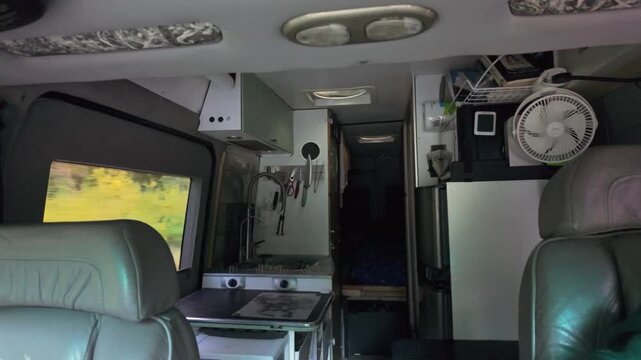 This scenic view captures the comfortable kitchen and living area inside an RV camper van as it travels through a lush forest