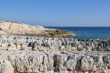 Rocky white cliffs and clear blue sea at Cape Kamenjak in Istria, with rugged stone formations and calm Adriatic waters under a bright sky.