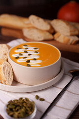 a cozy autumn scene with a bowl of creamy pumpkin soup topped with pumpkin seeds and cream, accompanied by slices of crusty bread, evoking warmth and comfort in a rustic setting, hot, piping, fall