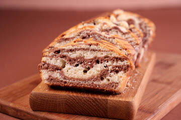 close-up slice of marbled cocoa and vanilla loaf cake on wooden board with warm brown background highlighting textured patterns and rustic presentation, yield, homely, presentation, sliced, gourmet