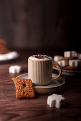 cozy scene with ceramic mug of foamy coffee, decorative cookie, and sugar cubes on wooden surface in warm ambient light, quiet, homey, artisanal, porcelain, crafted, surface, wooden, calm, inviting