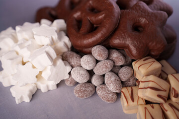 a tempting assortment of sweet snacks featuring chocolate-covered treats, powdered almonds, creamy fudge squares, and star-shaped marshmallows on a muted backdrop, treat, contrast, layered, gathered