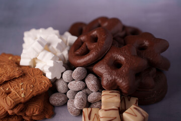assorted cookies and sweets: chocolate-covered treats, marshmallows, and spiced biscuits on a soft purple background, evoking cozy and indulgent dessert pleasure, classic, enticing, luxurious