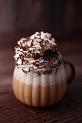 close-up of a creamy coffee topped with whipped cream and chocolate sprinkles in a textured glass mug on a wooden surface, creating a warm and inviting atmosphere, satisfying, savory, focus, ambient