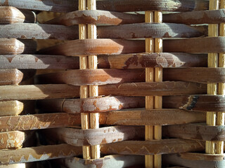 Macro close-up of thick rustic brown wicker basket weave texture in bright sunlight. Worn splintered natural fiber, handmade craftsmanship, wood, woven, rattan, light and shadow, detail, depth.