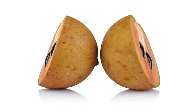 Sapodilla fruit cut in half with seeds on white background.