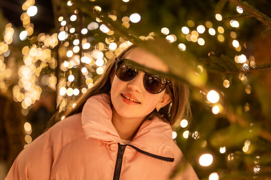 A surprised young teenage girl wearing sunglasses at a Christmas market in Europe. In the background, bokeh from the lights, with reflections of the market lights in her sunglasses.