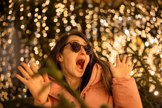 A surprised girl wearing sunglasses at a Christmas market in Europe. In the background, bokeh from the lights, with reflections of the market lights in her sunglasses.