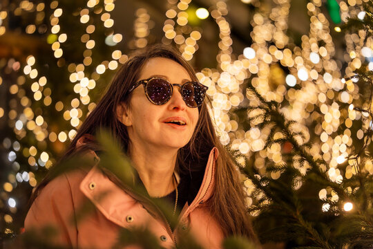 A surprised girl wearing sunglasses at a Christmas market in Europe. In the background, bokeh from the lights, with reflections of the market lights in her sunglasses.