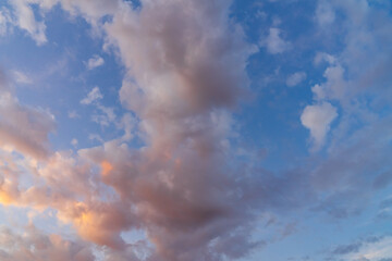 Vibrant evening sky with soft, scattered altocumulus clouds painted in hues of pink, orange, and golden sunlight against a deep blue background.