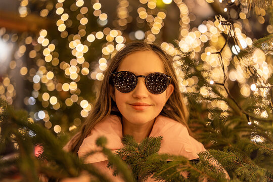 A surprised young teenage girl wearing sunglasses at a Christmas market in Europe. In the background, bokeh from the lights, with reflections of the market lights in her sunglasses.