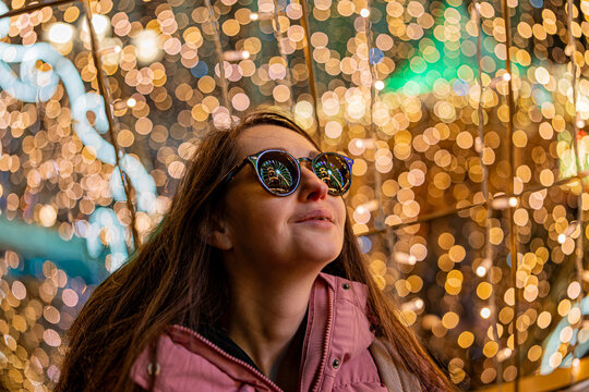 A surprised girl wearing sunglasses at a Christmas market in Europe. In the background, bokeh from the lights, with reflections of the market lights in her sunglasses.