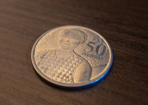 A Ghanaian 50 pesewas coin on a dark wooden table. It features the portrait of activist Rebecca Naa Dedei Aryeetey alongside the bold "50 PESEWAS" denomination in a silver metallic finish.