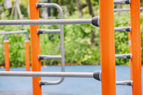 Modern outdoor gym equipment featuring orange columns and metal bars for calisthenics and bodyweight exercises in a public park