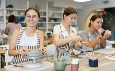 Young woman teacher and two girls students sculpt from clay and paint pottery