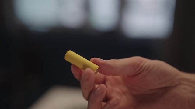 Male hand holding battery, examining yellow aa battery representing essential source of power and energy for various electronic devices, highlighting technology and electricity use, close-up.