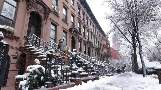 alt wide shot of man shoveling snow on stoop in front of Brooklyn brownstones