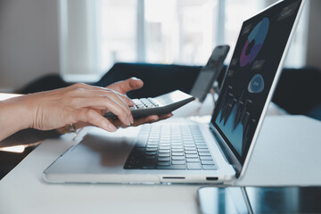 Closeup of woman using calculator and laptop with financial graphs on screen, representing data analysis, accounting, finance report, digital business, fintech, statistics, and performance metrics.
