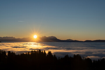 Obraz premium sunset over the summits of high mounatins above a sea of fog towards clear blue and orange sky in late autumn