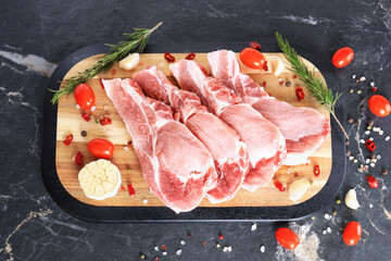 Fresh raw pork chops with rosemary, tomatoes, and garlic on a wooden board ready for cooking.