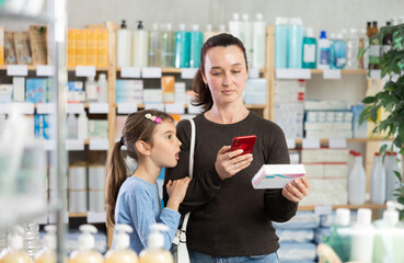 Woman with a child scans the barcode of a package of pills for children. Buyer pays for goods in the pharmacy using the online application