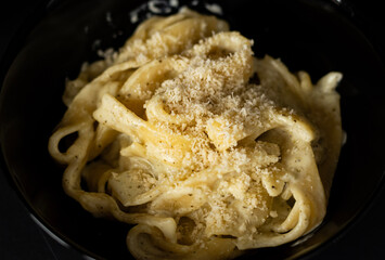 Creamy pasta with grated cheese served in a black bowl .