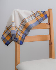A folded white handkerchief with a yellow, blue, and black plaid border is draped over the wooden backrest of a chair.