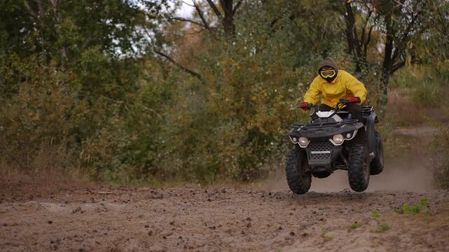 Slow motion. ATV rider in yellow jacket racing through muddy forest trail kicking up dust and stones, closeup jumps and wheel spray, dynamic camera angle, autumn foliage