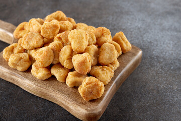 Crispy chicken popcorn on a wooden serving board against a gray background. Close-up. Fast food and snack concept.
