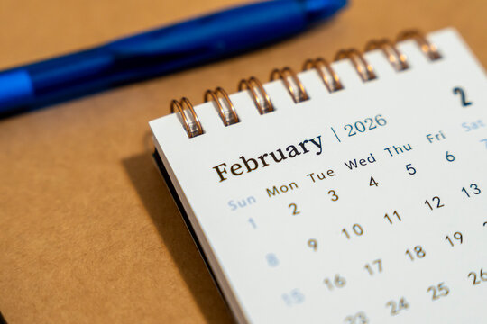Close-up view of a desk calendar displaying the month of February 2026 with a blue pen nearby. Ideal for concepts related to schedules, planning, and time management in professional contexts.