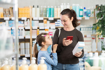 Adult woman with daughter buyers scanning qr code for moisturizing cream in pharmacy